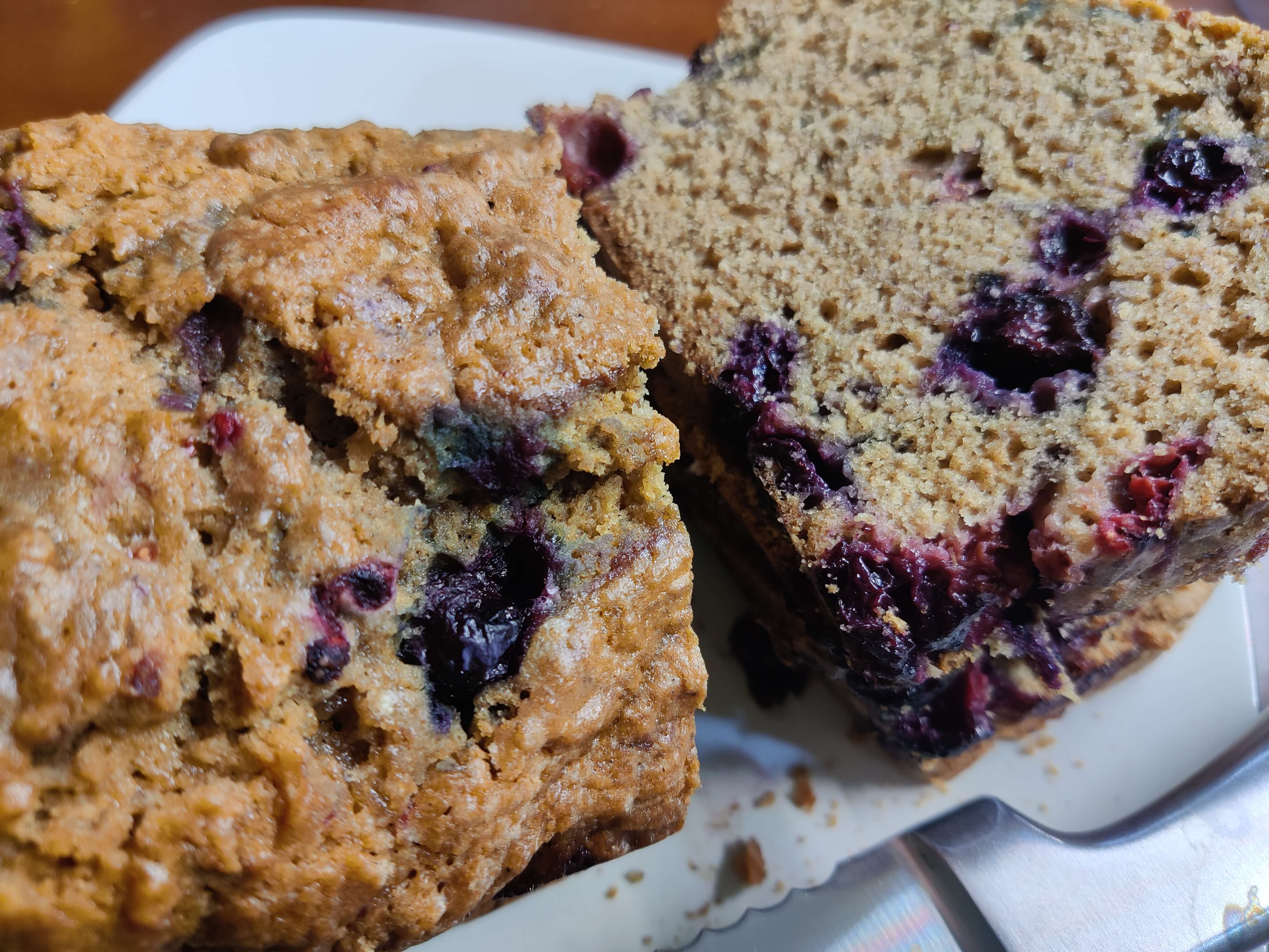 A close-up photo of the bread, which has a craggy, golden brown top dotted with berries and an interior with a dense crumb.